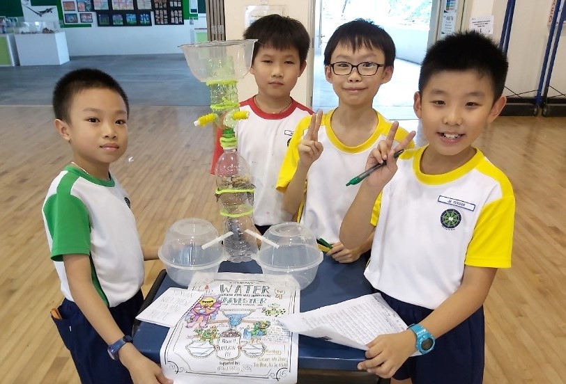 As part of their environmental science ALP, students designed their own rainwater harvester out of recycled materials. Here’s the team proudly showing how their prototype works! (Photo taken before COVID-19)