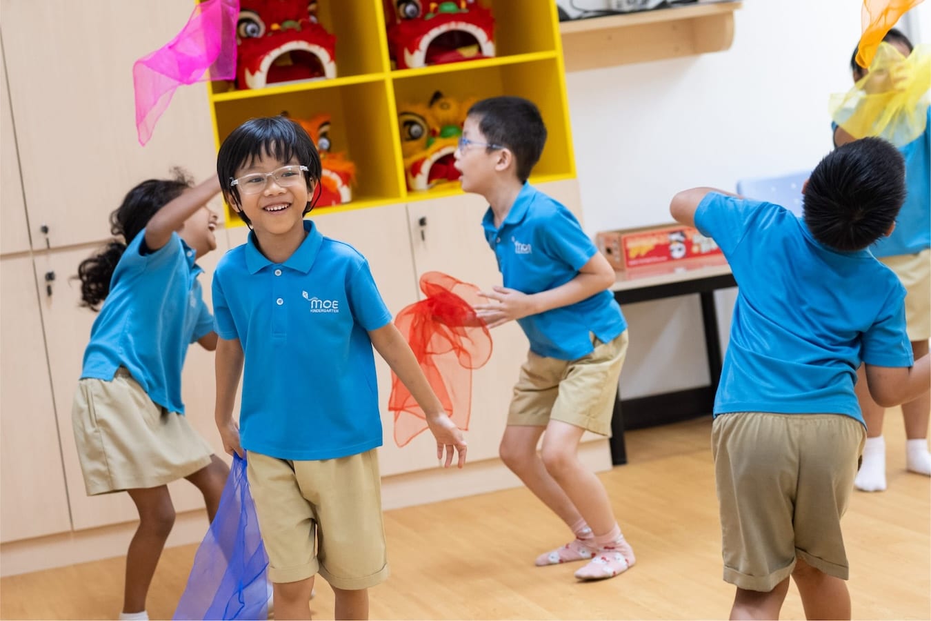 kindergarteners having fun dancing with thin, translucent pieces of coloured fabric